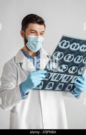 Homme médecin dans le masque de protection regardant l'image d'IRM avec radiographie des poumons Banque D'Images