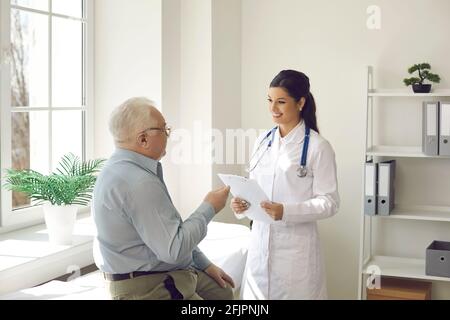Médecin souriant à l'écoute d'un patient âgé qui est assis à l'examen lit dans son bureau Banque D'Images
