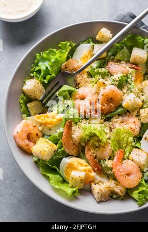 Salade de crevettes. Salade César aux fruits de mer servie avec des croûtons, de la sauce césar et du parmesan dans un bol proche. Banque D'Images