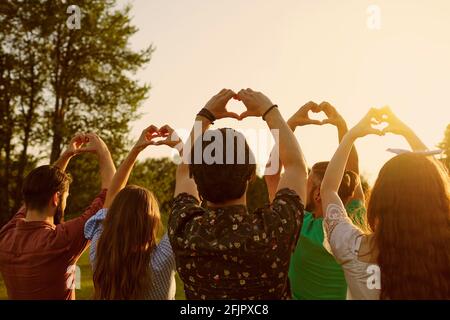 Signe main coeur. Un groupe de personnes tient les mains avec un signe de coeur sur un fond de ciel avec coucher de soleil sur la nature. Banque D'Images