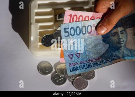 Un enfant asiatique tient de l'argent indonésien, avec le fond de la boîte à monnaie, dans un foyer peu profond. Concept d'enregistrement et de don. Banque D'Images