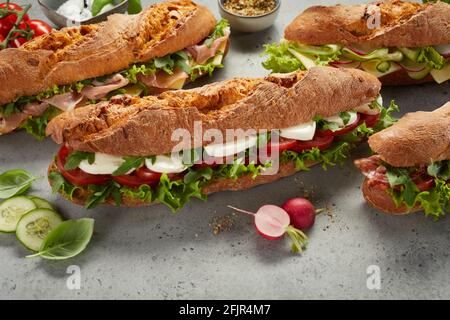 Gros plan d'un délicieux sous-marin avec du fromage mozzarella et du rouge frais tomates avec laitue et arugula placées au milieu de divers types de sandwichs Banque D'Images