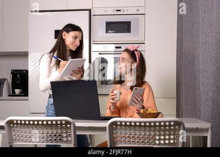 Deux amis dans une cuisine se rattraper et s'amuser tout en étudiant sur un ordinateur portable. Formation à distance. Banque D'Images