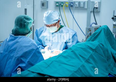 Les chirurgiens et un assistant utilisent les instruments qui opèrent l'os dans le bras du patient dans la salle d'opération. Médecins professionnels en exercice Banque D'Images