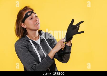Portrait d'une femme cambrioleur dans un masque, portant des gants. Arrière-plan jaune. Le concept de la criminalité. Banque D'Images