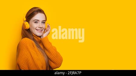 Belle femme de gingembre écoute de la musique sur un jaune mur avec espace libre souriant à l'appareil photo Banque D'Images