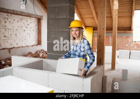 une jolie jeune femme de travail avec un casque de sécurité jaune travaille dessus chantier et pose un mur intérieur dans un maison Banque D'Images