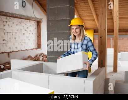 une jolie jeune femme de travail avec un casque de sécurité jaune travaille dessus chantier et pose un mur intérieur dans un maison Banque D'Images