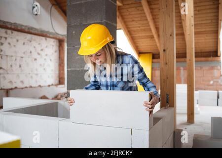 une jolie jeune femme de travail avec un casque de sécurité jaune travaille dessus chantier et pose un mur intérieur dans un maison Banque D'Images