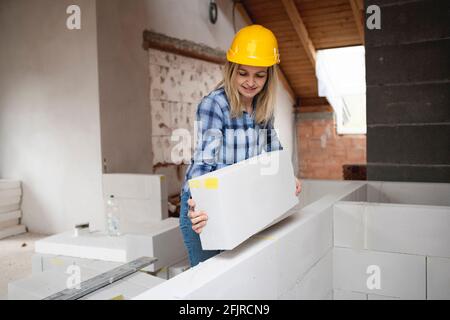 une jolie jeune femme de travail avec un casque de sécurité jaune travaille dessus chantier et pose un mur intérieur dans un maison Banque D'Images