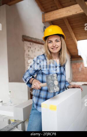 une jolie jeune femme de travail avec un casque de sécurité jaune travaille dessus chantier et pose un mur intérieur dans un maison Banque D'Images