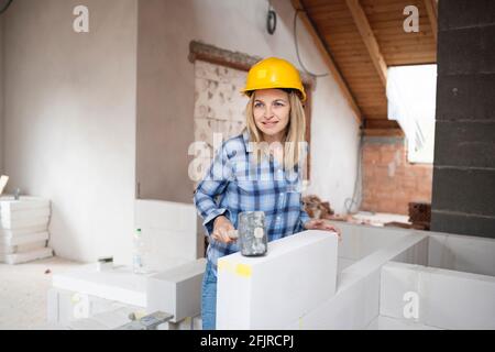 une jolie jeune femme de travail avec un casque de sécurité jaune travaille dessus chantier et pose un mur intérieur dans un maison Banque D'Images