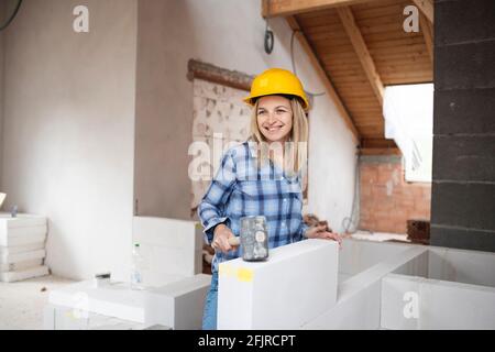 une jolie jeune femme de travail avec un casque de sécurité jaune travaille dessus chantier et pose un mur intérieur dans un maison Banque D'Images