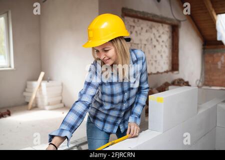 une jolie jeune femme de travail avec un casque de sécurité jaune travaille dessus chantier et pose un mur intérieur dans un maison Banque D'Images