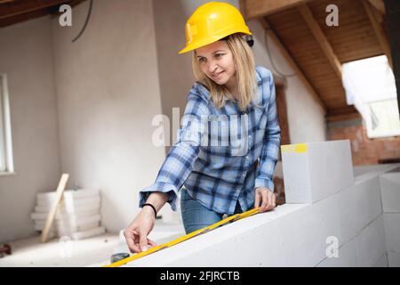 une jolie jeune femme de travail avec un casque de sécurité jaune travaille dessus chantier et pose un mur intérieur dans un maison Banque D'Images