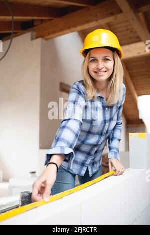 une jolie jeune femme de travail avec un casque de sécurité jaune travaille dessus chantier et pose un mur intérieur dans un maison Banque D'Images