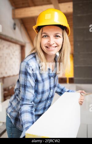 une jolie jeune femme de travail avec un casque de sécurité jaune travaille dessus chantier et pose un mur intérieur dans un maison Banque D'Images