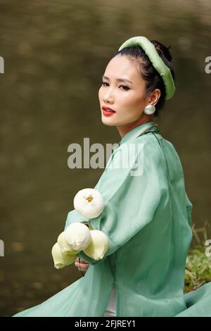 Charmante jeune femme en robe traditionnelle vietnamienne et coiffures repos par l'eau le jour d'été Banque D'Images