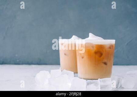 Café glacé en verre avec mousse de lait et glaçons sur table blanche, espace de copie... Banque D'Images