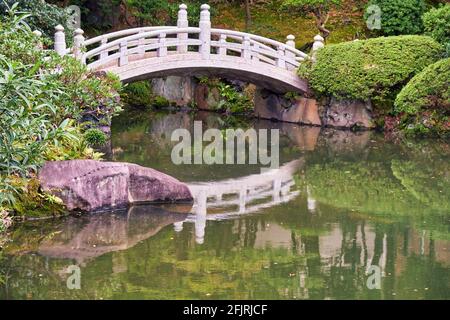 Pont d'arche blanc au-dessus de l'étang au centre de l'ancien jardin Yasuda (Kyu-yasuda Teien), un petit jardin de promenade japonais situé à Ryogoku. Tokyo. Japon Banque D'Images