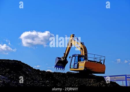 Creuseur mécanique sur un monticule contre le ciel bleu sur un chantier Banque D'Images