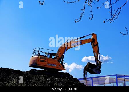 Creuseur mécanique sur un monticule contre le ciel bleu sur un chantier Banque D'Images