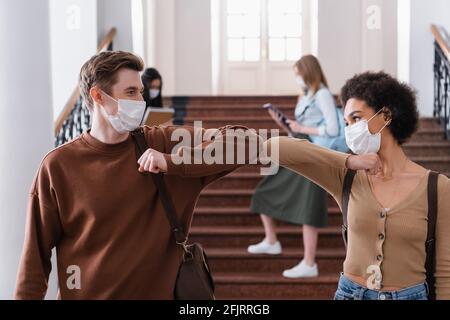 Les étudiants multiethniques dans les masques médicaux saluent avec la bosse du coude Banque D'Images