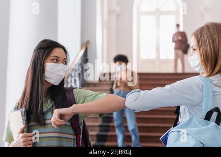 Les étudiants multiethniques dans les masques médicaux saluent avec la bosse du coude Banque D'Images