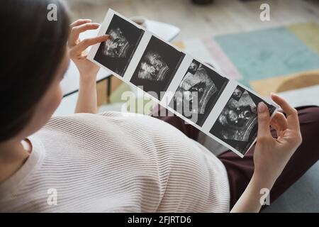 Femme enceinte assise sur un canapé avec des images radiographiques qu'elle regarde à l'échographie de son bébé Banque D'Images