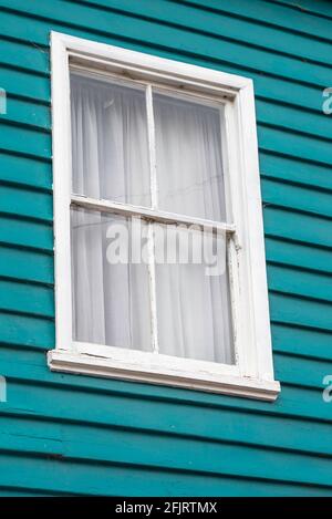 Une fenêtre en bois anonyme peint en blanc légèrement abîmé un mur en bois bleu-vert dans une maison avec des rideaux dessiné Banque D'Images