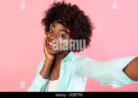 Jolie femme noire faisant Selfie visage en contact sur fond rose Banque D'Images