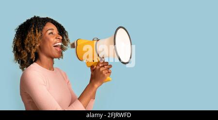 Concept d'annonce. Joyeuse Black femme criant avec Megaphone dans les mains, fond bleu Banque D'Images