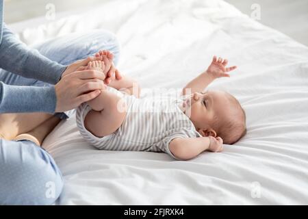 Mère bienveillante faisant de la gymnastique à son nouveau-né bébé sur le lit À la maison Banque D'Images