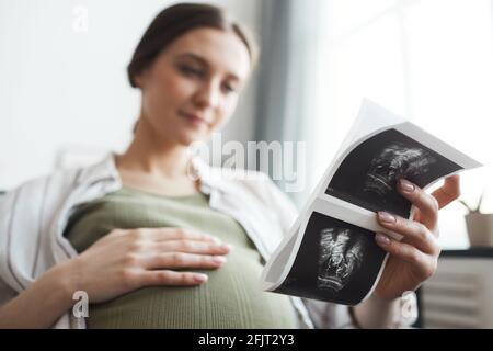 Femme enceinte tenant une image radiographique de son bébé pendant son accouchement reposez-vous sur le canapé à la maison Banque D'Images