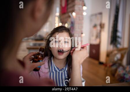 Mère s'occuper de petite fille malade à la maison, donnant du sirop. Banque D'Images