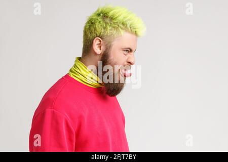 Profil de l'homme insouciant puéril avec la barbe robes chandail rouge montrant la langue et la fabrication du visage, a l'expression désobéissante. Indo Banque D'Images