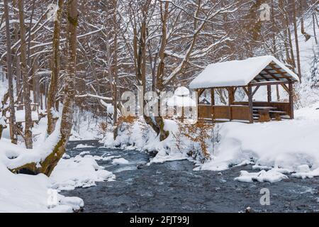 Un petit belvédère en bois dans les profondeurs d'une forêt d'hiver près d'un ruisseau de montagne froid et noyés marchent le long de lui, grimpant d'une vallée forestière Banque D'Images