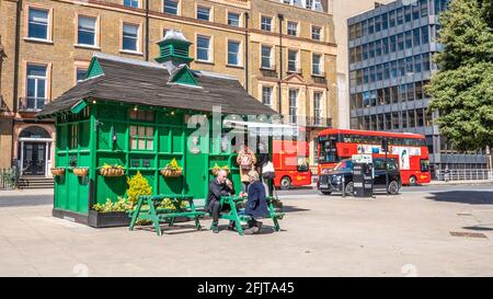 London Cabmen's Shelter. Un bâtiment historique qui fournit traditionnellement un refuge aux chauffeurs de taxi. Un taxi électrique moderne se recharge en arrière-plan. Banque D'Images