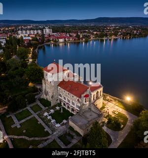 Tata, Hongrie - vue panoramique aérienne du magnifique château illuminé de Tata (Tati var) au bord du vieux lac (Oreg-to) au crépuscule avec un ciel bleu clair Banque D'Images