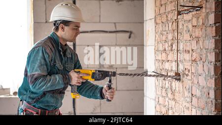 Handyman dans le processus de perçage d'un mur avec un perforateur. Banque D'Images