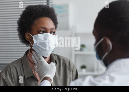 Femme africaine en masque de protection assis au bureau du médecin pendant médecin examinant sa gorge Banque D'Images