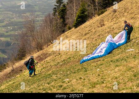 Les hommes sur une pente herbeuse préparent le planeur pour le parapente depuis le refuge ERE. San Gregorio nelle Alpi, Belluno, Italie Banque D'Images