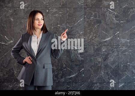 Jeune brune en costume gris d'affaires, points à l'espace de copie. Banque D'Images