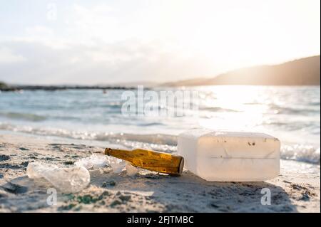 Bouteilles en plastique et déchets sur le rivage, pollution de la plage. Eau de mer et coucher de soleil sur fond. Banque D'Images