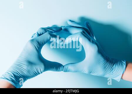 Figure coeur construit avec les mains dans des gants médicaux sur fond bleu. Copier l'espace. Journée nationale des médecins. Journée internationale des infirmières. Protection de la santé Banque D'Images