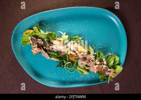 salade de thon et d'herbes sur une assiette turquoise vue du dessus. Banque D'Images