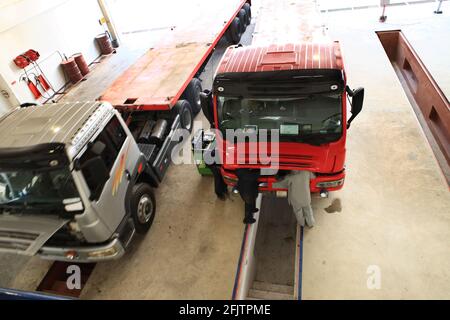 Un groupe de mécaniciens travaille sur 2 camions garés dans un garage de réparation pour les poids lourds. Banque D'Images