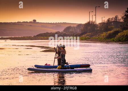 Feu d'or en soirée, deux planchistes femelles sur les paddleboards Stand Up paddle à marée haute sur la rivière Gannel à Newquay dans les Cornouailles. Banque D'Images