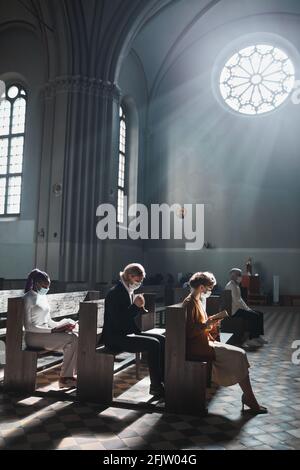 Groupe de personnes assis sur le banc dans la vieille belle église priant ensemble pendant une messe Banque D'Images