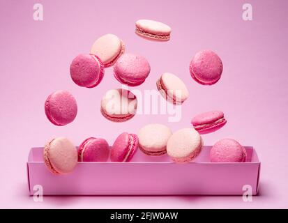 Macarons doux colorés ou macarons, biscuits aromatisés flottant dans l'air au-dessus de la boîte en papier. Banque D'Images